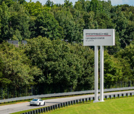 a white Porsche drives along a race track as it passes a large white sign for Porsche North America