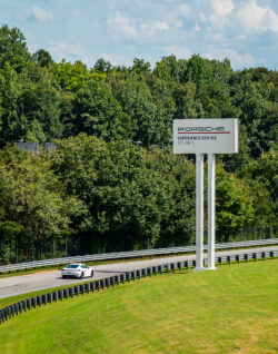 a white Porsche drives along a race track as it passes a large white sign for Porsche North America